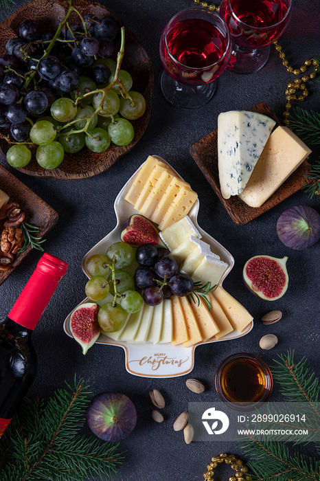 Variety of cheese and fruits served in plate as Christmas tree, on dark gray background with two gla