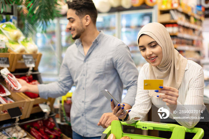 Islamic Couple Doing Grocery Shopping Using Smartphone In Store Indoors