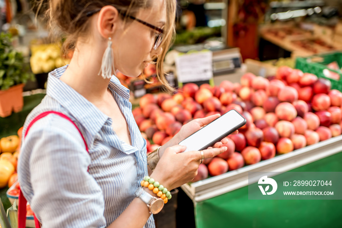 Young woman using smartphone standing with bag in front of the food market in France