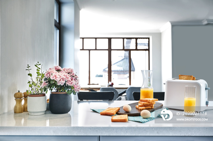 Toaster with fresh toast, eggs and glass of orange juice on a light kitchen table