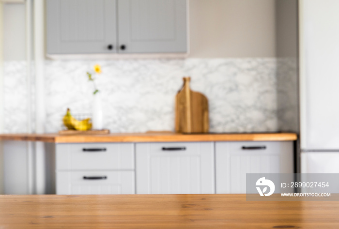Selective focus on empty natural wooden kitchen table, blurred gray kitchen furniture on background.