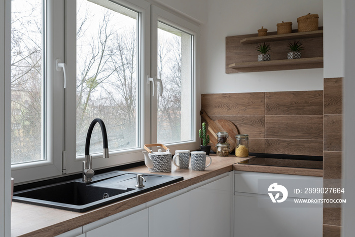 Kitchen sink with faucet near the window. White modern furniture and wooden tiles on the wall in sty