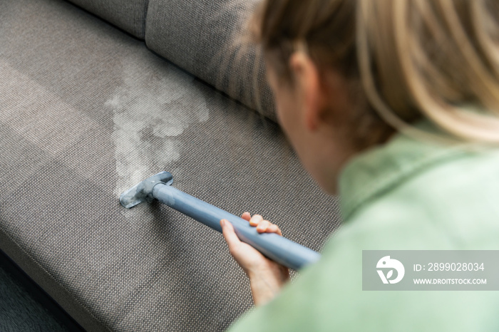 woman cleaning fabric sofa with a steam cleaner at home