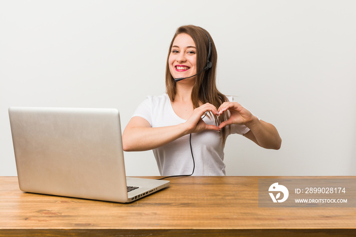 Young telemarketer woman smiling and showing a heart shape with hands.