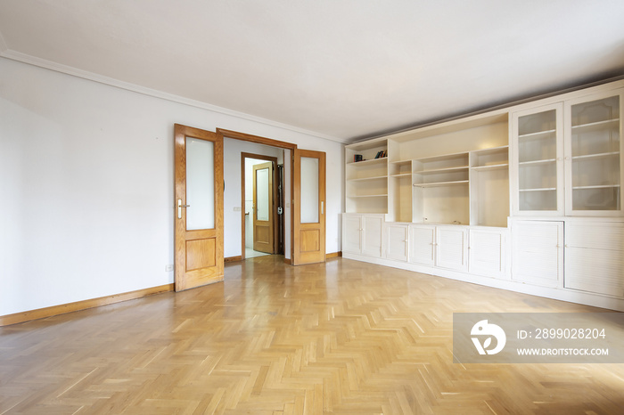 Empty living room with French parquet floors, pine wood double doors and white bookcase with Venetia