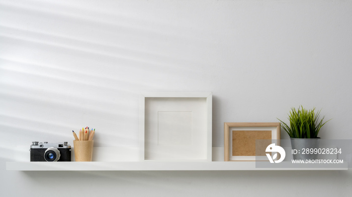 Close up view of mock up frames, camera and decorations on white shelf with white wall background