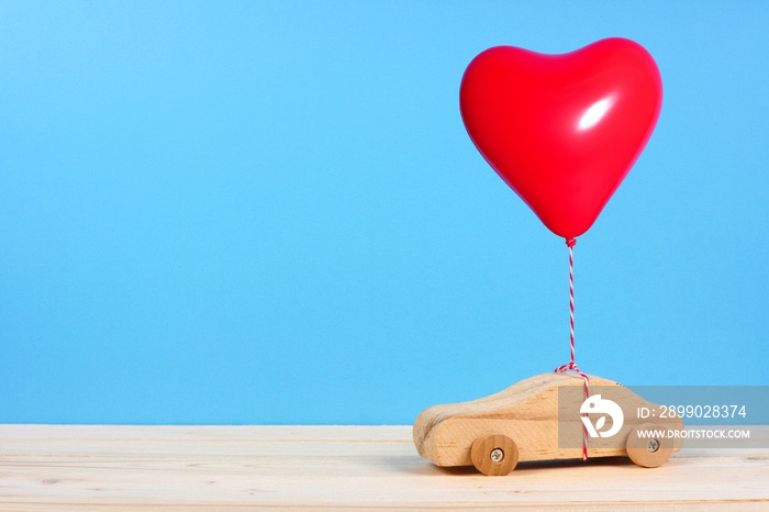 Wooden toy car with a red heart balloon against a blue background. Valentines Day or love concept.