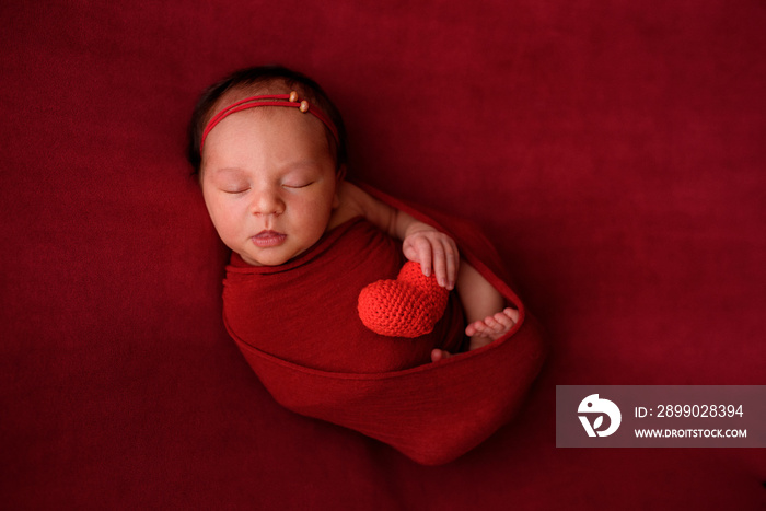 Newborn girl sleeping on a red cloth in a red wrapper