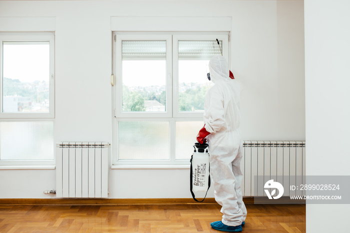 Exterminator in work wear spraying pesticide or insecticide with sprayer