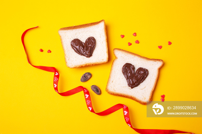 Two heart shaped toast bread sandwiches with chocolate spread on a yellow background. Flat lay style