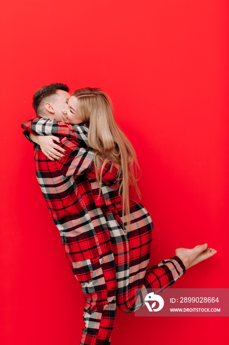 Happy Saint Valentines Day. Young couple in the same pyjamas is kissing and hugging on red backgrou