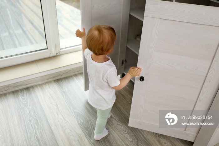 Cute baby girl playing with a wooden cupboard