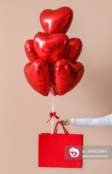 Woman with paper bag and heart-shaped balloons for Valentines Day near beige wall