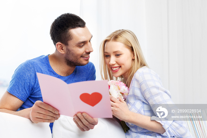 love, valentines day and people concept - happy couple with greeting card and flowers at home