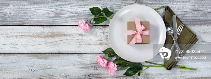 Dinner setting with pink roses and gift on rustic white wood