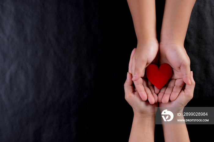 Woman hand giving red heart to child. International day of charity or love concept. Copy space.