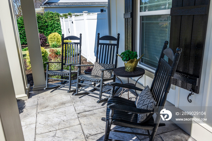 A stamped concrete gray front porch with black rocking chairs sitting in the front for curb appeal