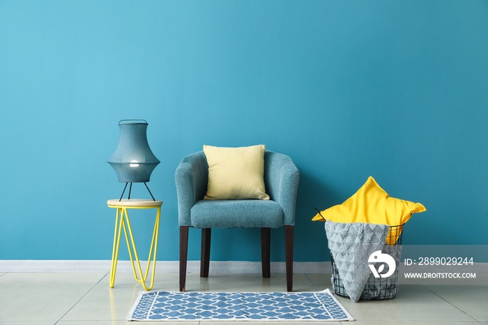 Stylish coffee table with lamp, armchair and basket near blue wall