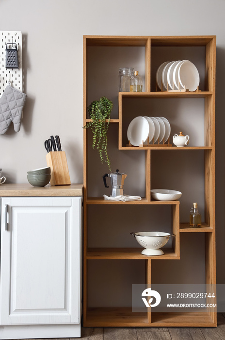 Wooden shelving unit with dishware, coffee maker and houseplant near light wall in kitchen