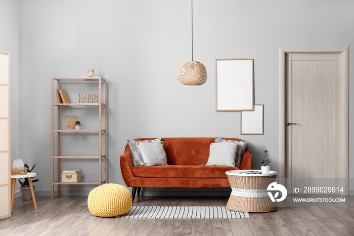 Interior of modern room with comfortable sofa, pouf and blank photo frames on light wall