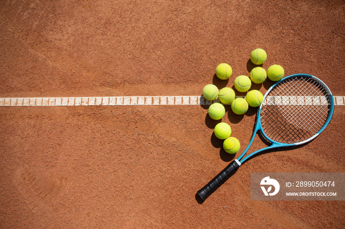 Top view of racket and twelve balls while they are lying on sunny court. Outfit is being used for training sport skills. Copy space in left side