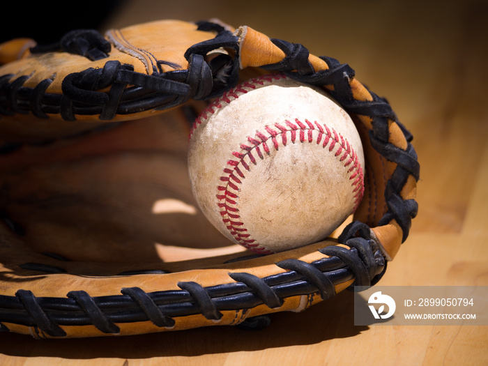 Close up sports background image of an old used weathered leather baseball with red laces inside of a baseball glove or mitt showing intricate detailing and black leather lacing.