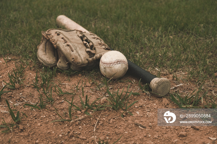 Old baseball with glove and bat lay on sports field.