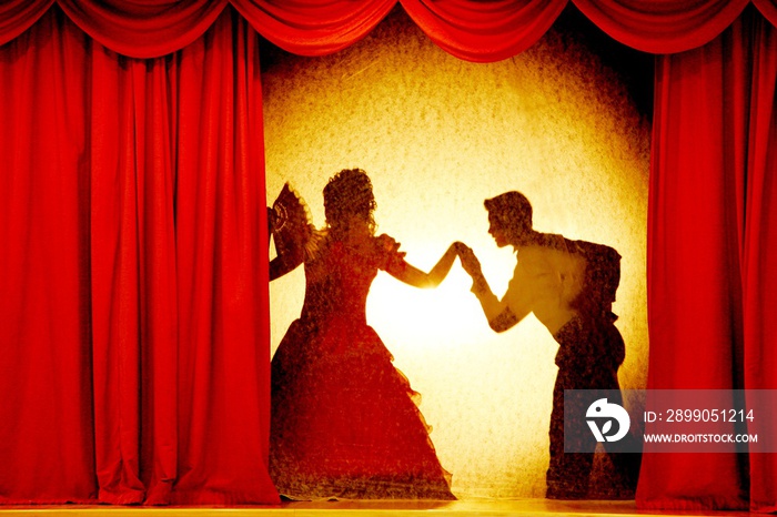 A man and woman in theatrical costumes in the theater of shadows on the stage with red curtains. Love in the shadows theatre. Red curtain of opera, cinema or theater stage drapes.