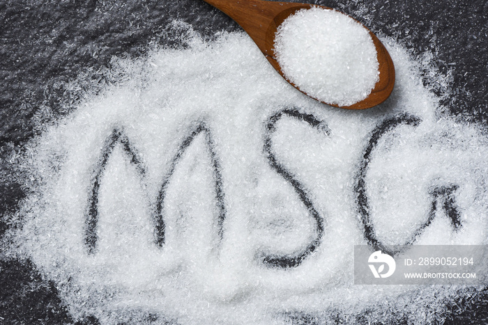 Heap of monosodium glutamate on wooden spoon and dark background - text MSG