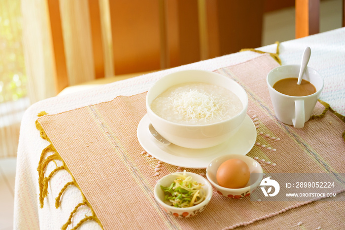 rice porridge, rice gruel or congee with pork, egg, sliced ginger and vegetable, delicious the traditional Chinese breakfast on wooden table and hot coffee