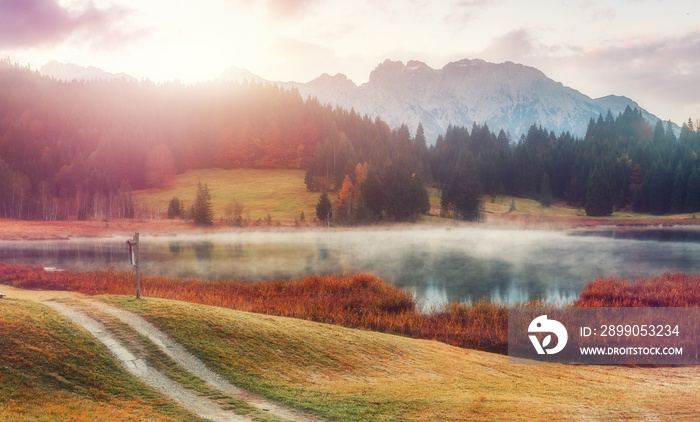 Womderful Autumn landscape. Road on meadow with grass on top view. Fairy Alpine lake Geroldsee with morning fog under sunlit. Dramatic Impressive scene. Amazing nature background