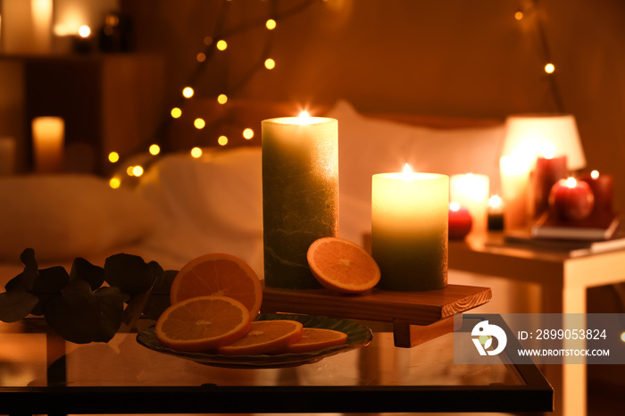 Wooden board with burning candles and sliced orange on table in room