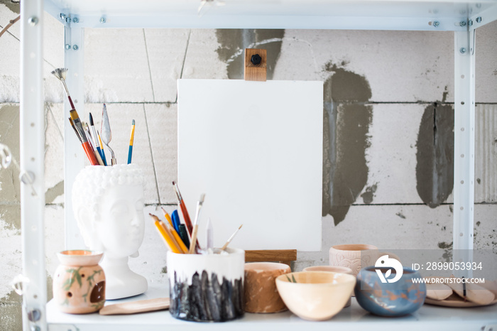 Pencils, canvas and brushes on shelf in artistic studio