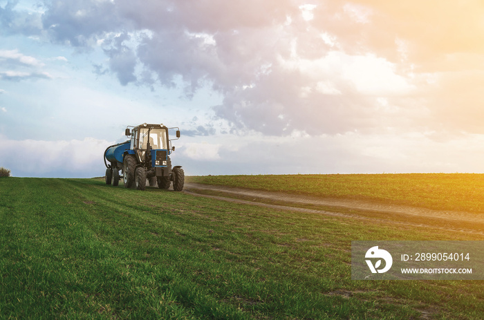 Tractor with a barrel trailer rides on a green field