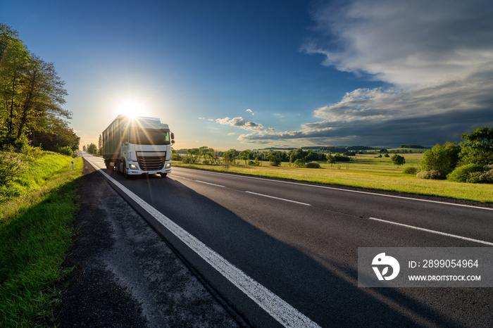 White truck driving on the asphalt road in rural landscape in the rays of the sunset