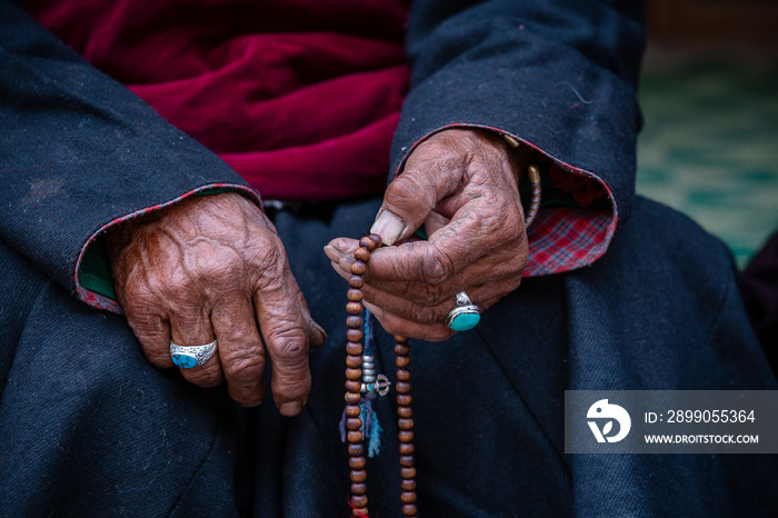 Old Tibetan woman holding Buddhist rosary in Hemis monastery, Ladakh, India. Hand and rosary