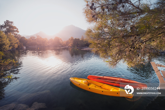 Two rowing boats kayaks without people are bobbing on the waves moored to the shore with a view of the rising sun over the mountain