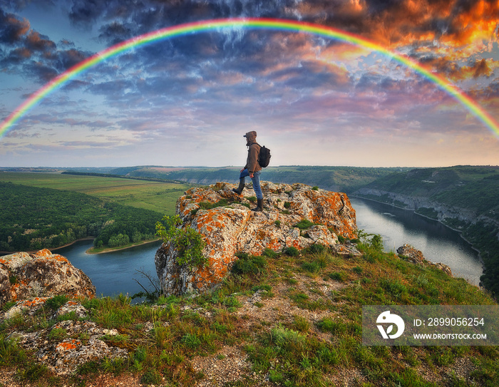 colorful rainbow over the river. man on a rock above the canyon