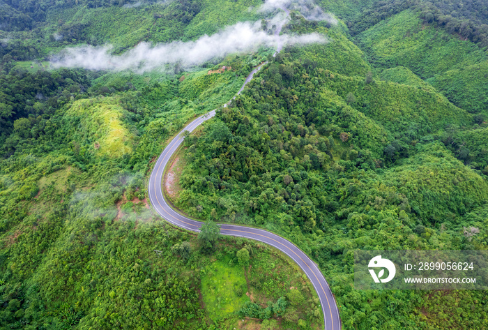 Top view of countryside road passing through the green forrest and mountain