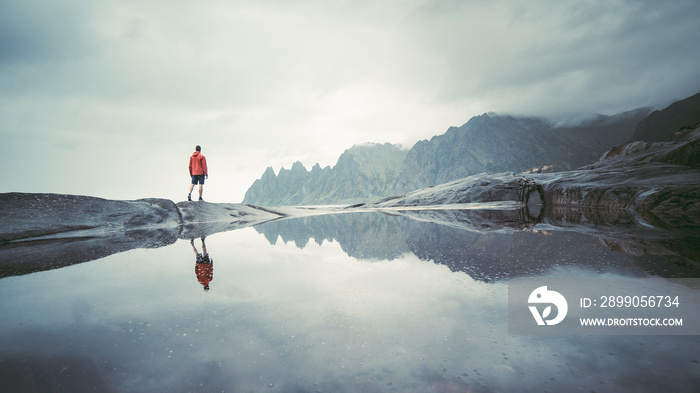 Adventurous man standing on stone. The Tungeneset rest area lies on the tip of the promontory that separates the Steinsfjord and the Ersfjord. Tungeneset Senja on the mirror refection, Norway