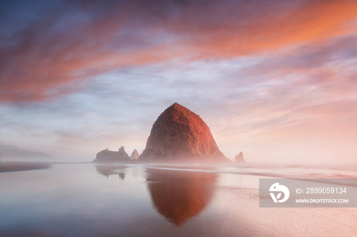 The Sunset at Cannon Beach with Dramatic clouds in the background and a nice reflection in water. Dramatic coastal seascape featuring scenic rock formations Haystack Rock Oregon, USA
