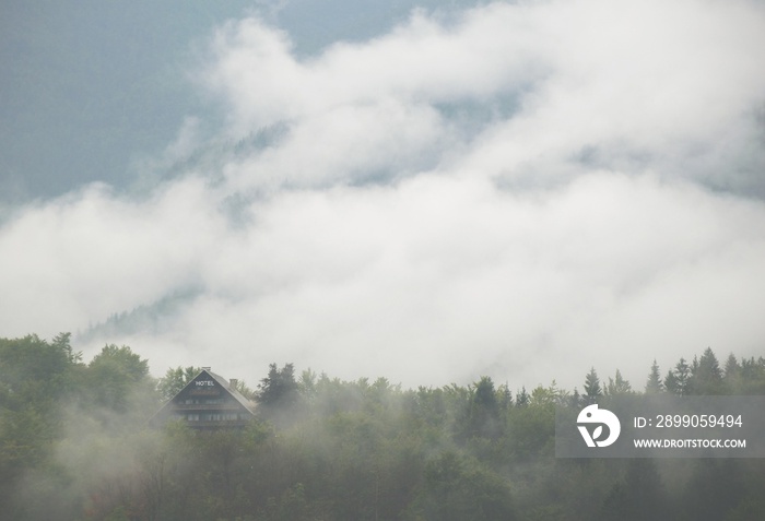 Hidden hotel in moody mountains. Building with many windows and HOTEL billboard sign on the top. Forest and passing clouds around Triglav nationalpark,Slovenia.