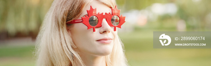 Beautiful blonde Caucasian young girl wearing canadian maple leaf sunglasses. Happy woman with funny red glasses. A citizen female celebrating Canada Day on July 1. Web banner header.