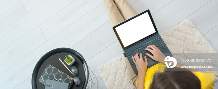 Top view of female freelancer sitting on floor near sofa at home and working on mockup laptop computer. Woman typing on laptop stay home. Quarantine concept work online