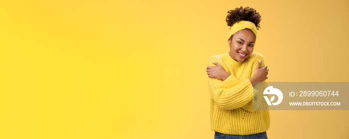 Attractive tender gentle african-american teenage girl in sweater headband hugging herself hands touch shoulders feel warm safe cozy smiling happily embracing cuddling lovely giggle