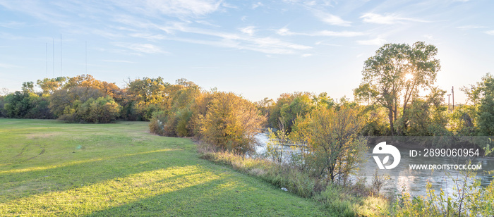 Panorama view beautiful riverside park with fall foliage vibrant color and sun peeking through trees in Carrollton, Texas, USA. Stunning yellow autumn leaves at sunset