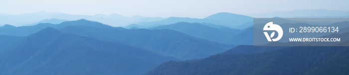 Panorama of dark blue mountain landscape in fog. Horizontal image. Selective focus.