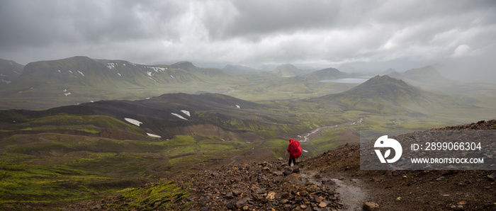 A person in a red rain cape hiking the Laugavegur trail in Iceland with a breathtaking view into a valley.