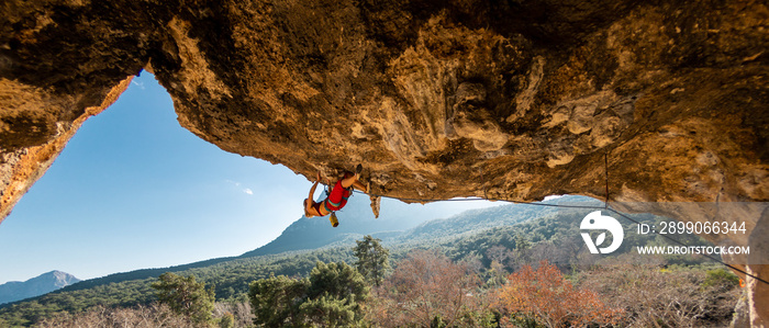 A young rock climber on an overhanging cliff. The climber climbs the rock. The girl is engaged in sports climbing.