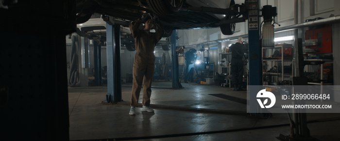 Caucasian female mechanic repairing a car in a workshop, working under car bottom